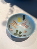 Ceramic bowl with painted ribbon forms in a soft blue glaze
